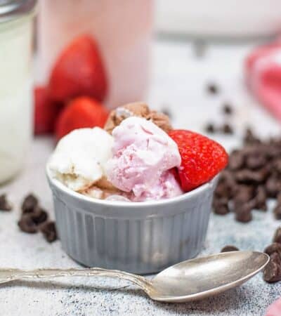 Mason jar ice cream in strawberry, vanilla, and chocolate scooped into a bowl and garnished with a fresh strawberry.