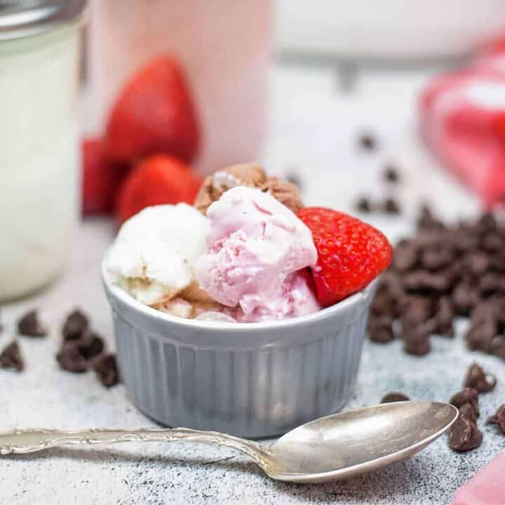 Mason jar ice cream in strawberry, vanilla, and chocolate scooped into a bowl and garnished with a fresh strawberry.