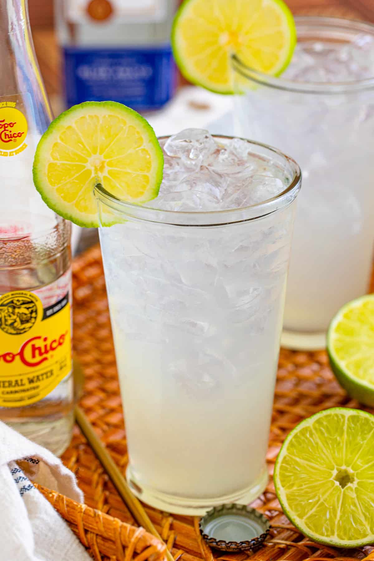 Ranch water drink with tequila, fresh lime, and Topo Chico on straw tray.