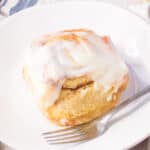 Large cinnamon roll with cream cheese icing on a white plate with a fork.