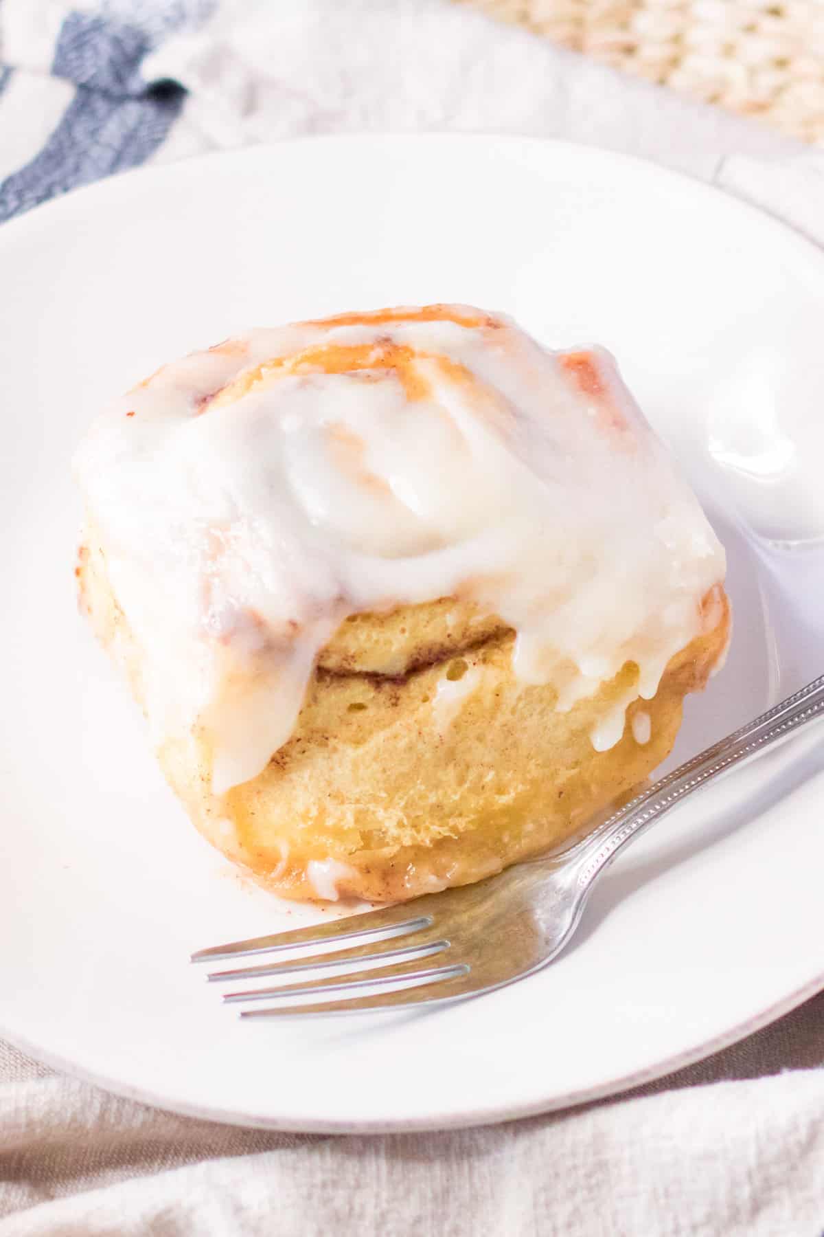 Large cinnamon roll with cream cheese icing on a white plate with a fork.