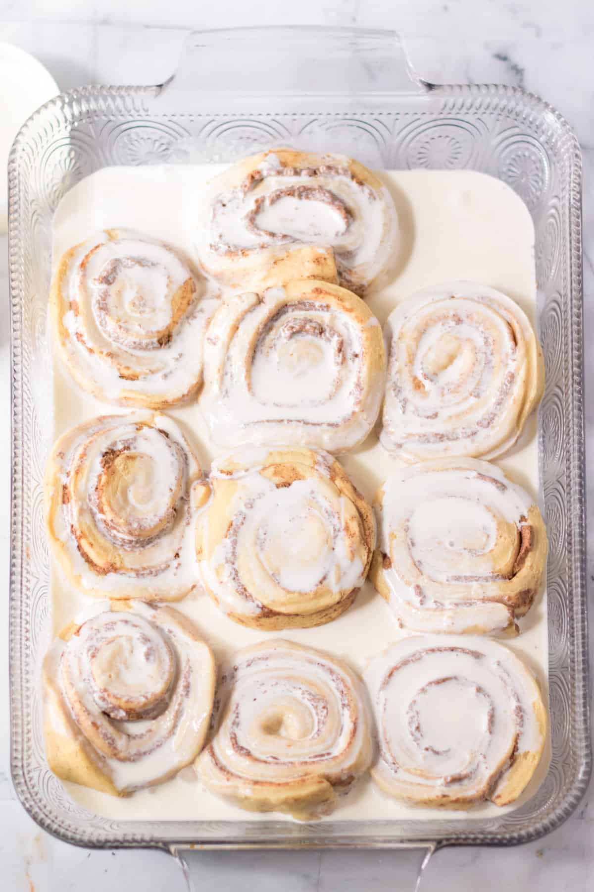 Cinnamon rolls in glass baking dish with heavy cream poured over them.