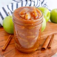 Apple pie filling in a wide mouth mason jar with cinnamon sticks and apples around it.