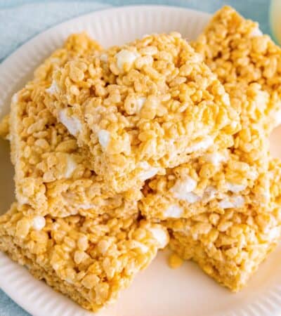 Bakery style rice krispies treats sliced into squares and piled on white plate.