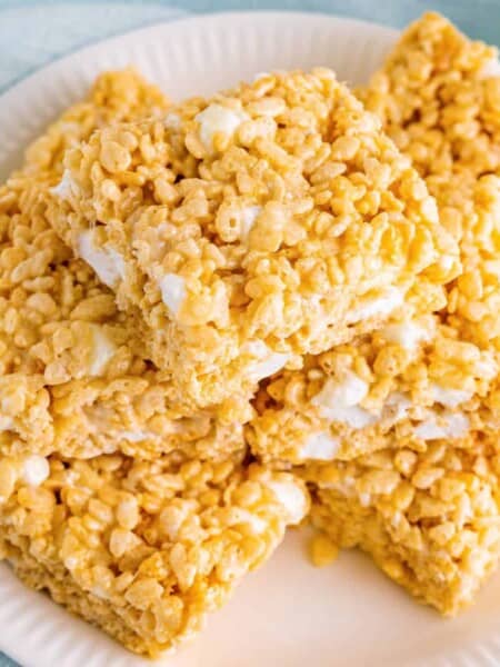 Bakery style rice krispies treats sliced into squares and piled on white plate.
