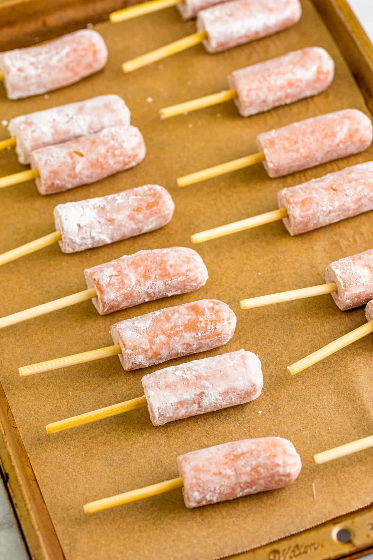 Halved hot dogs with wooded skewers on lined baking sheet.