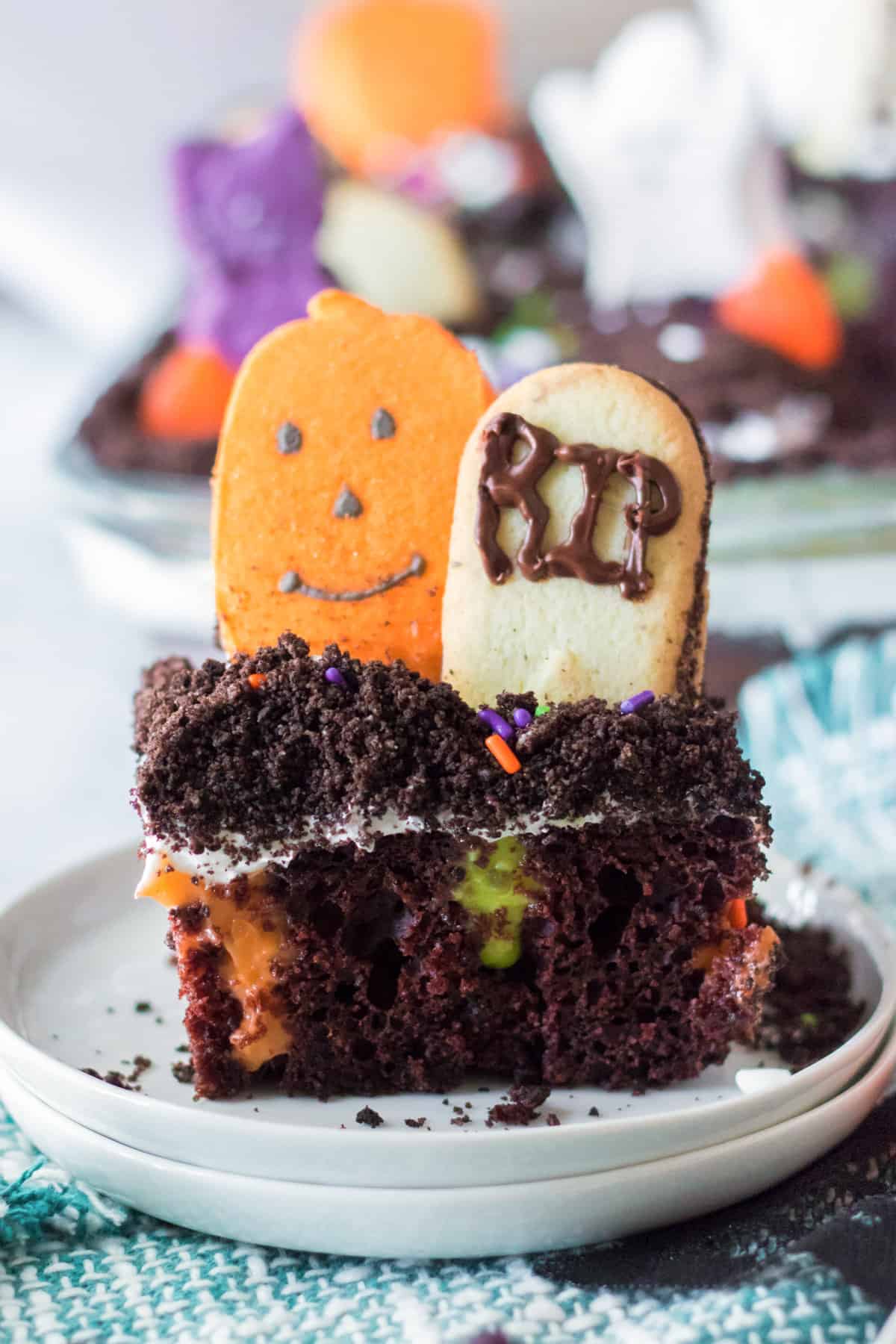 Piece of Ghosts in the Graveyard poke cake with cookie tombstone and candy pumpkin.