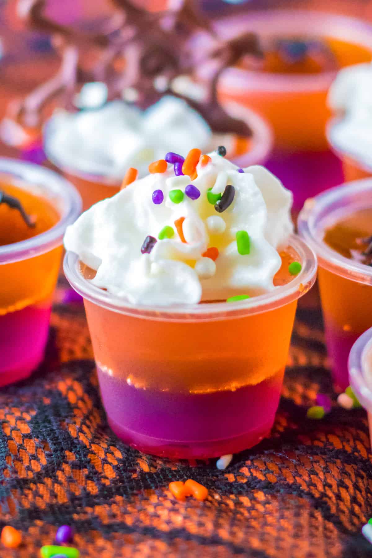 Purple and orange layered Halloween Jello Shots topped with whipped cream and sprinkles.