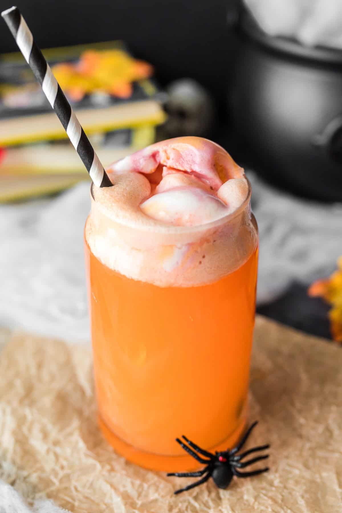 Orange hocus pocus punch for kids in glass with black and white straw.