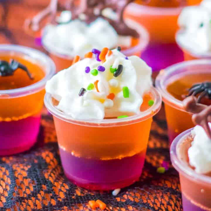 Purple and orange layered Halloween Jello Shots topped with whipped cream and sprinkles.