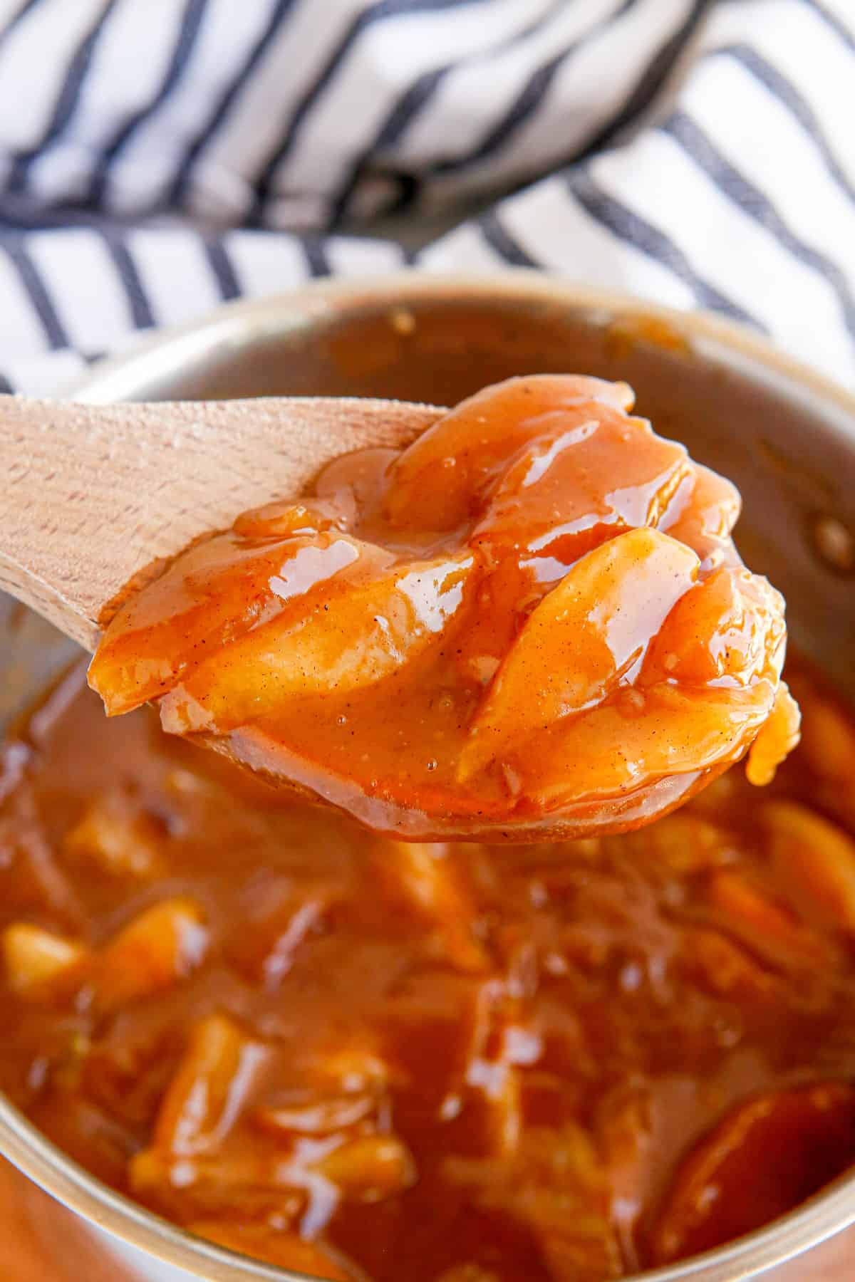 Wooden spoon lifting apple pie filling out of pot.