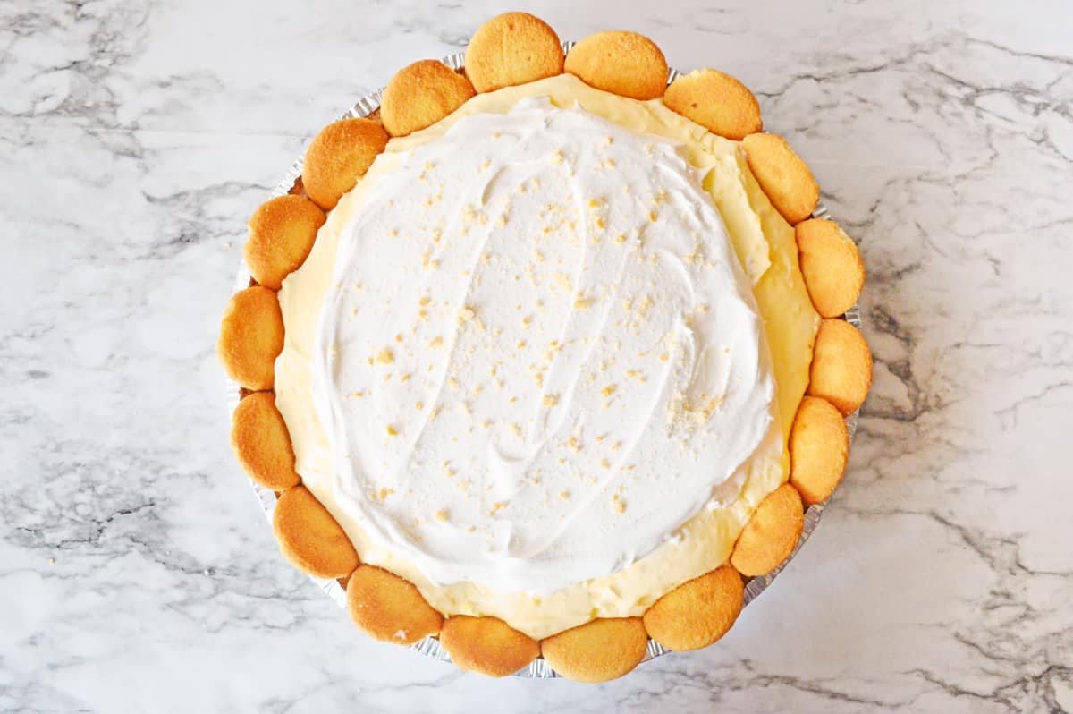Banana pie topped with whipped topping, nilla wafers, and nilla wafer crumbles.