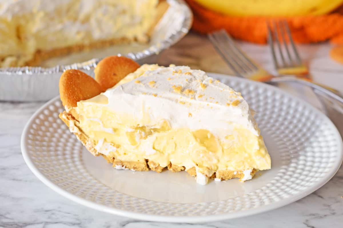 Slice of banana pudding pie on plate with remaining pie in background.