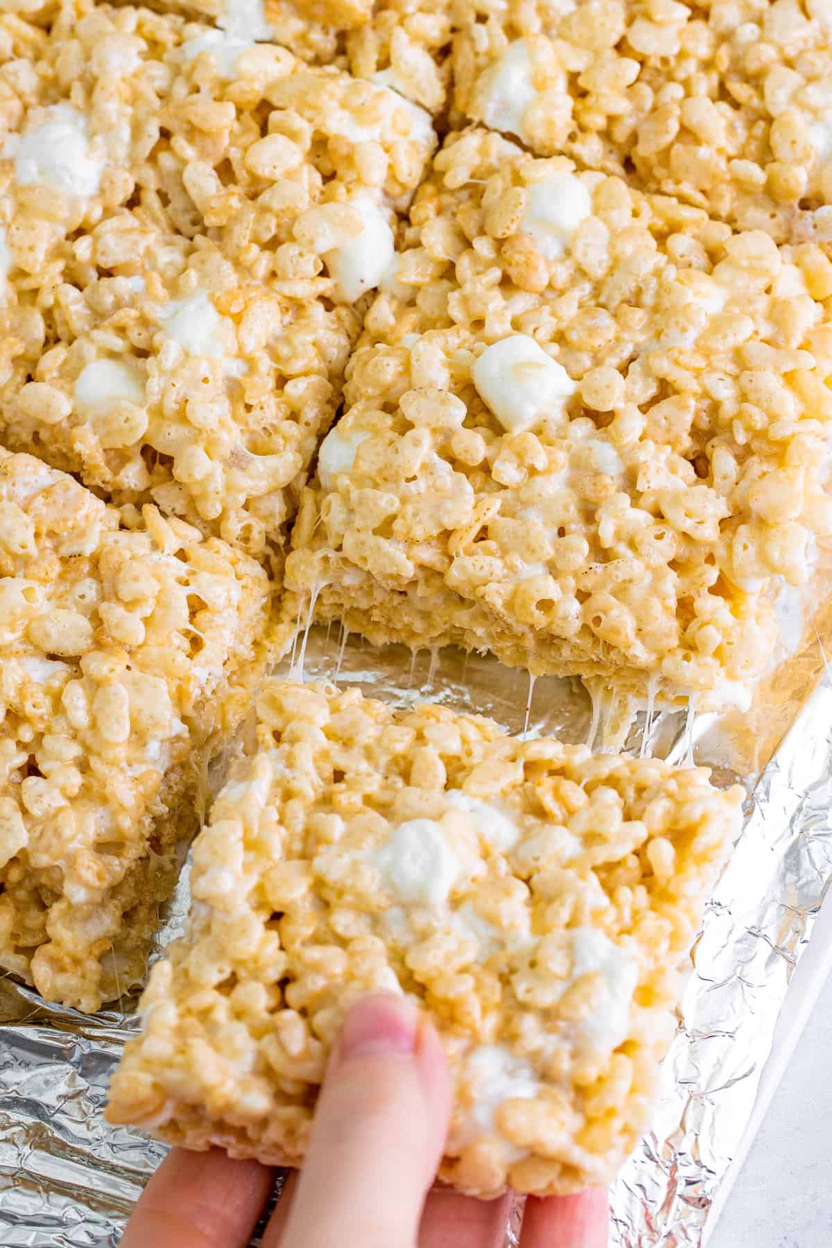 Gooey rice krispie treat being pulled from tray of treats.