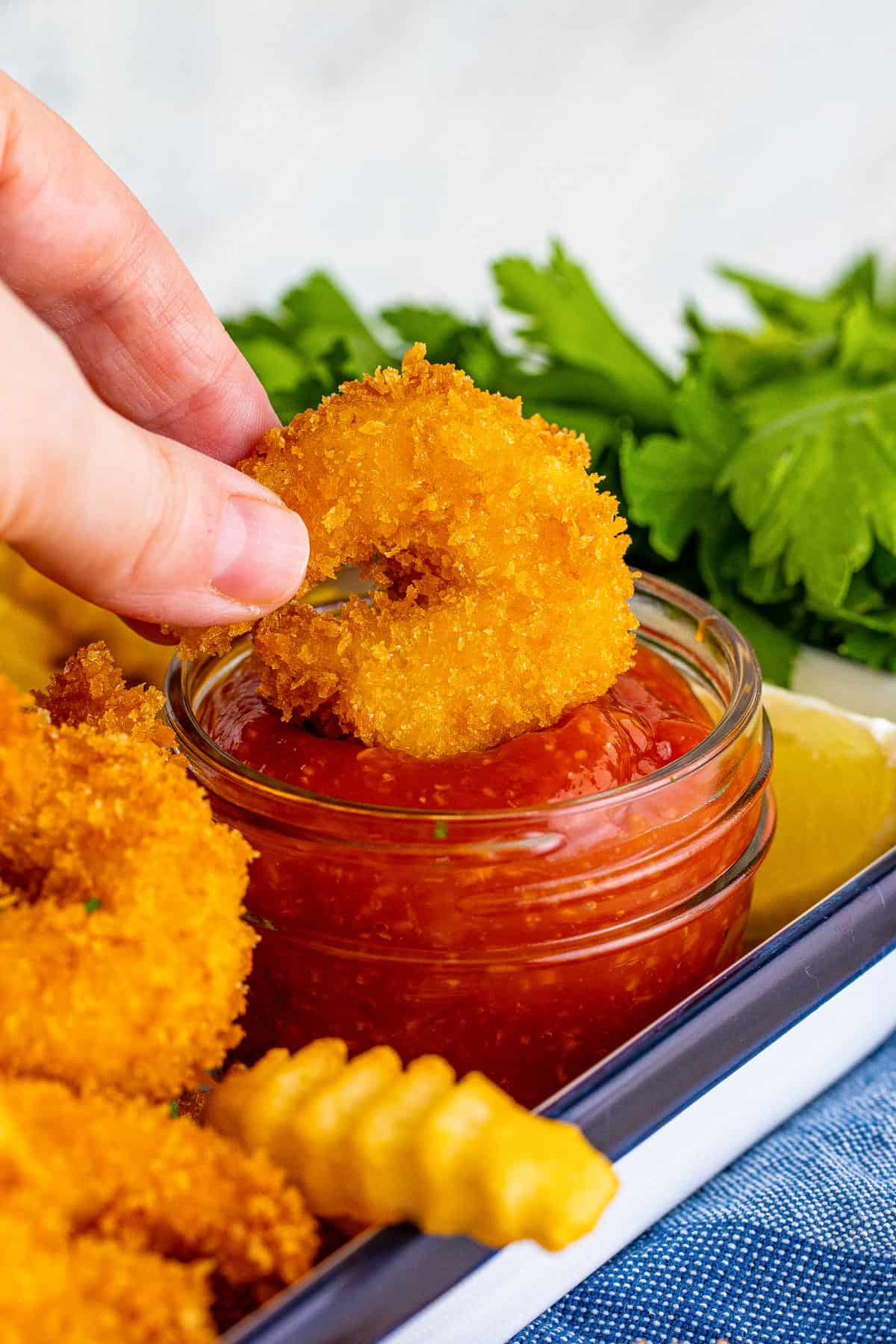 Panko fried shrimp being dipped in cocktail sauce.