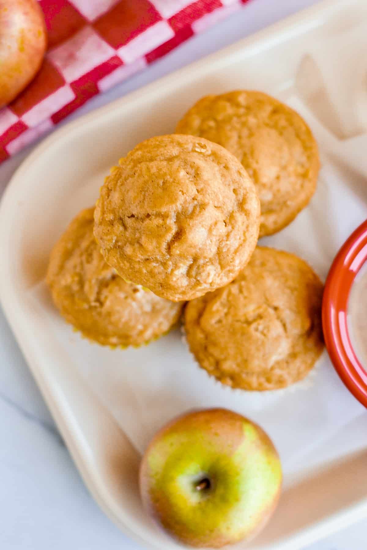 Apple oat muffins on lunch tray with fresh apple besides them.