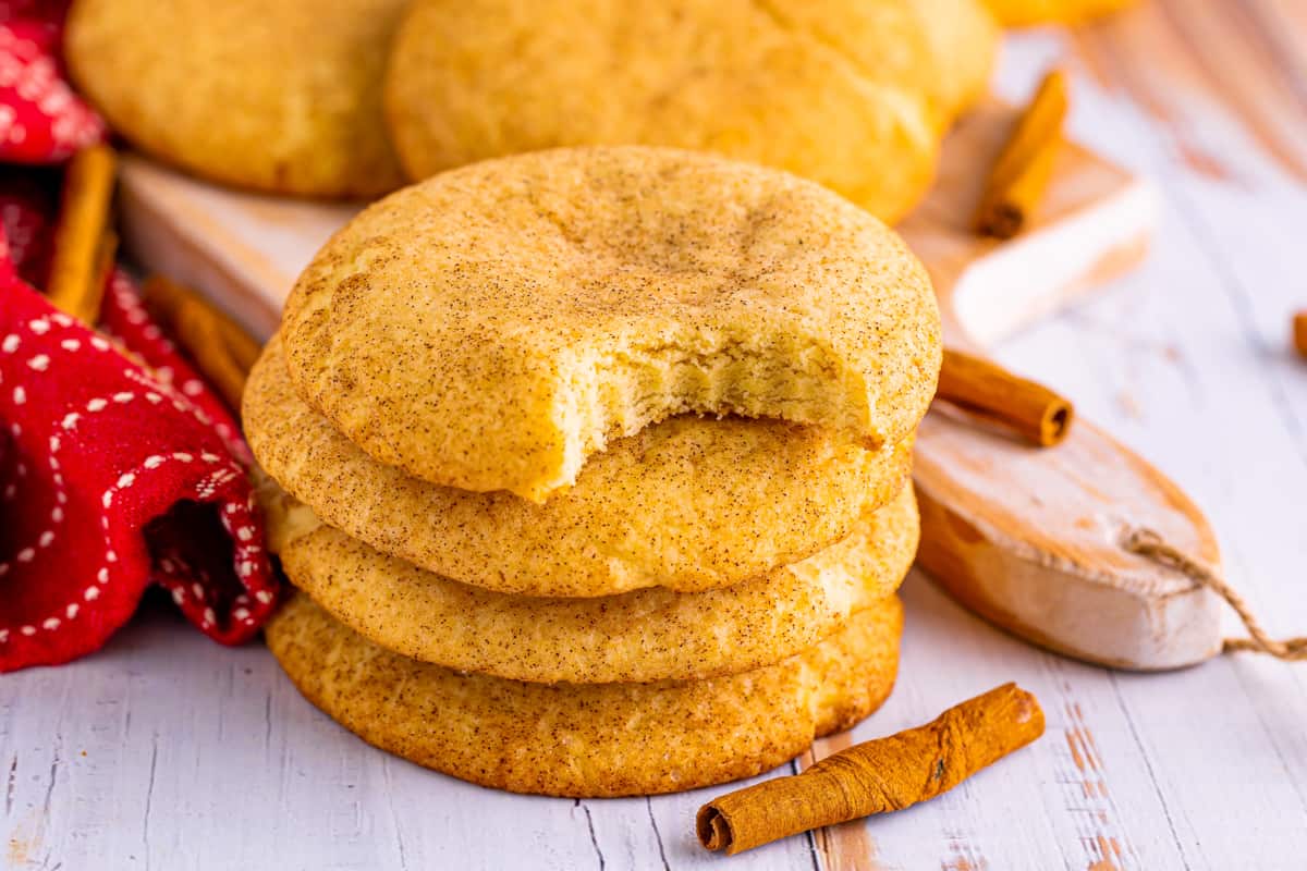 Thick and soft snickerdoodle cookies stacked on top of one another with a bite taken out of the top cookie.