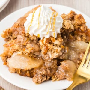 Apple crisp topped with dollop of whipped cream and caramel drizzle.