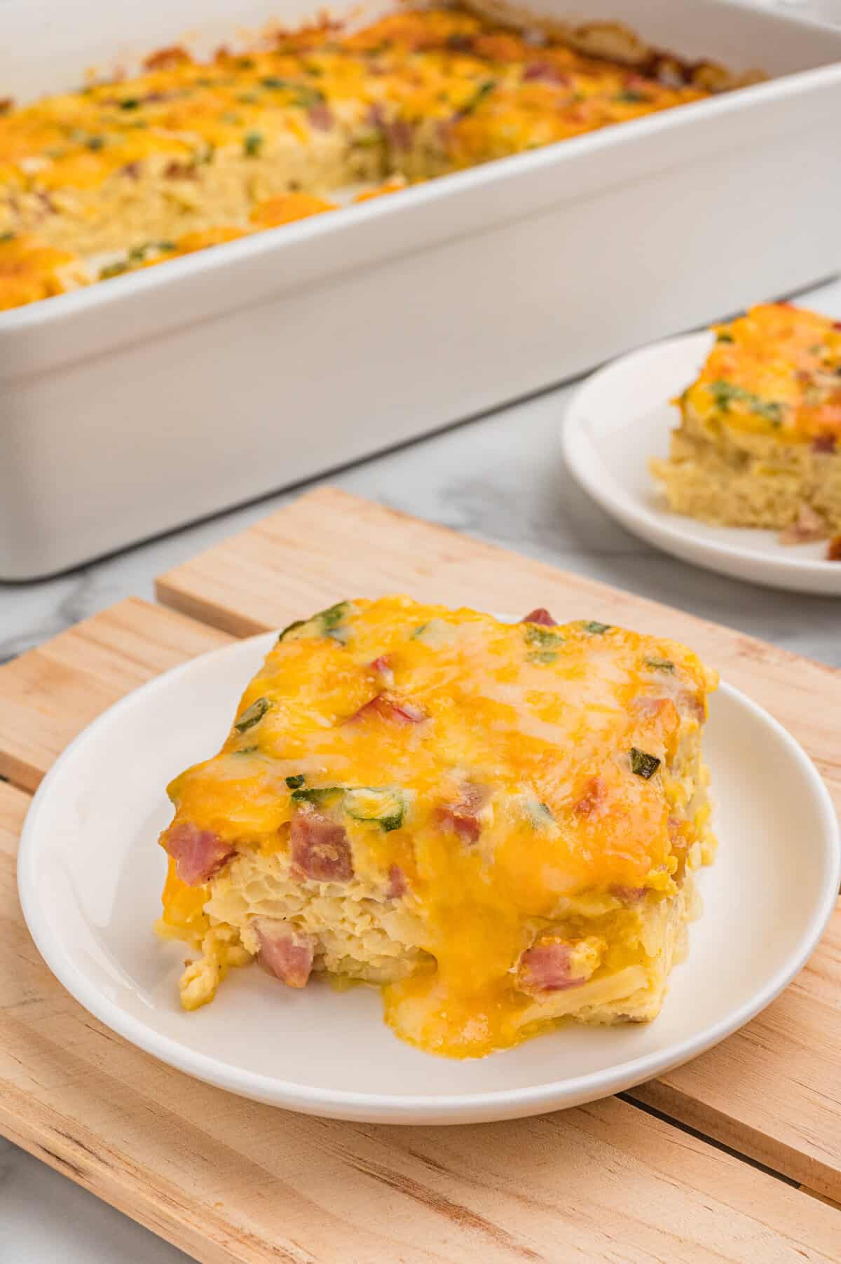 A slice of farmers casserole plated in front of the baking dish.