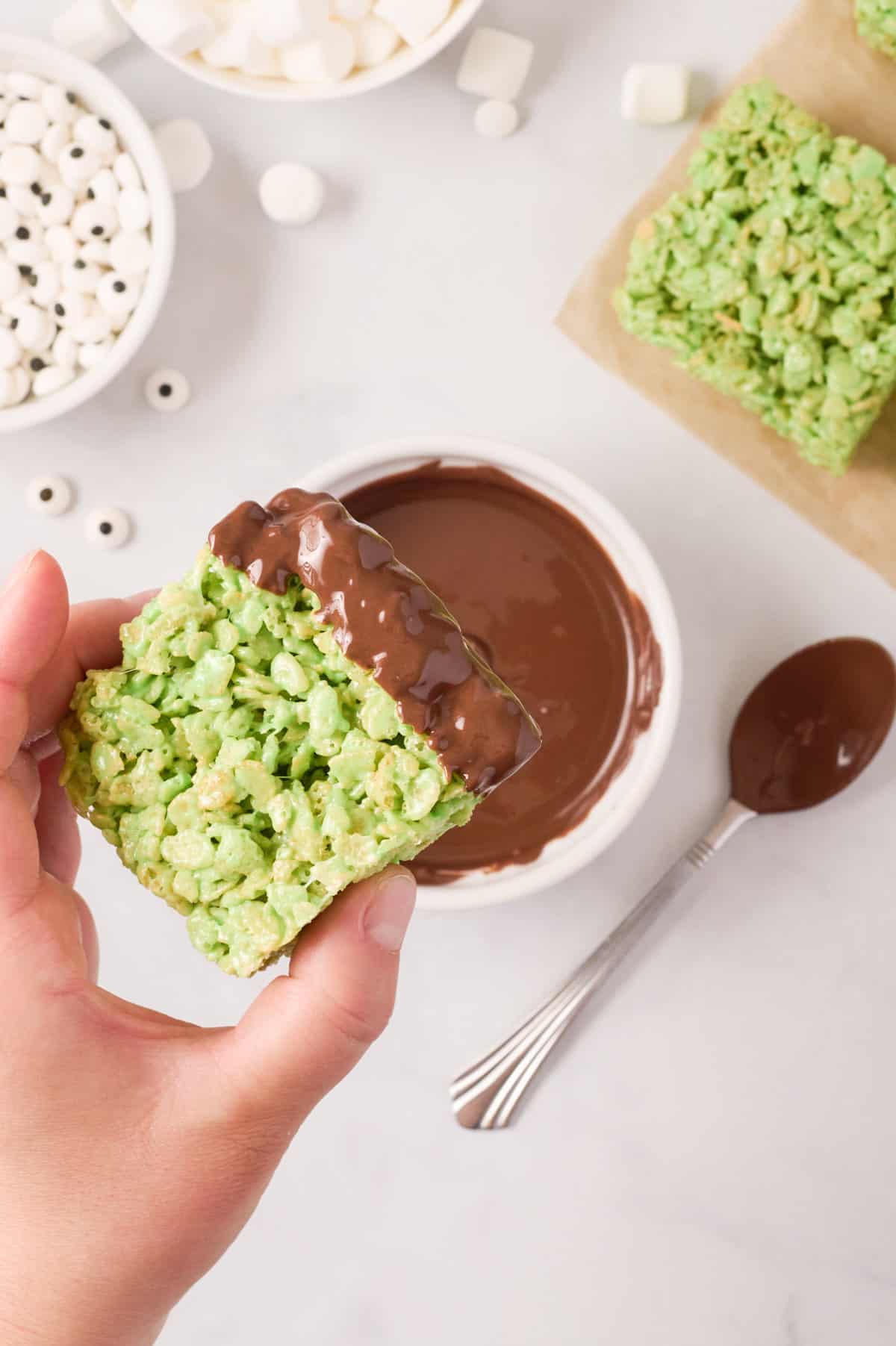 Green treat being dipped in bowl of melted chocolate.