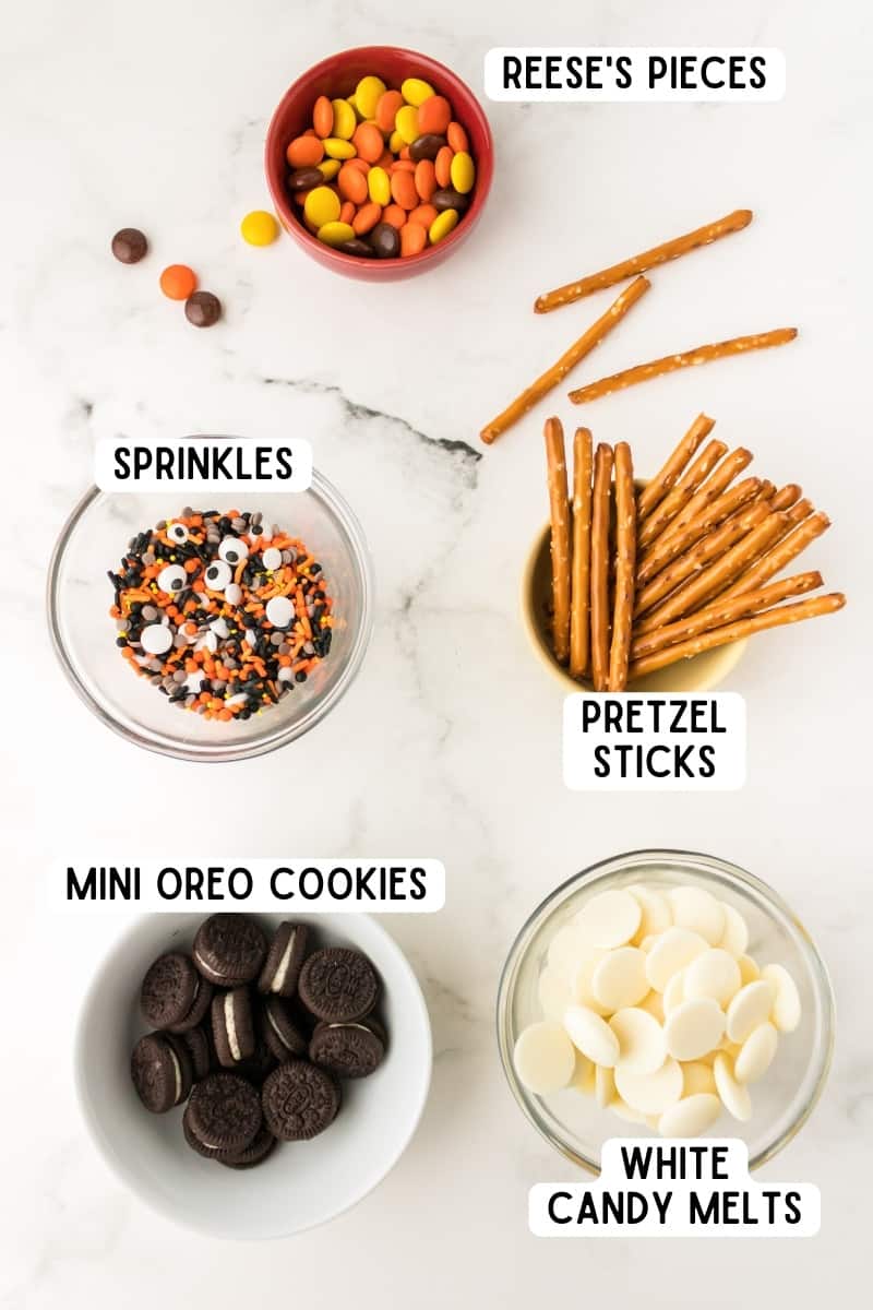 Ingredients for halloween bark recipe: pretzels sticks, reese's pieces, white candy melts, mini oreos.