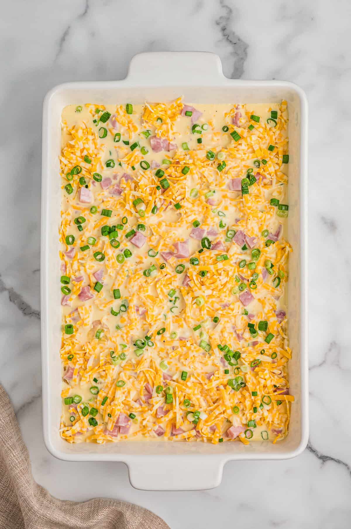 Breakfast casserole ingredients in casserole dish with egg mixture poured over them.