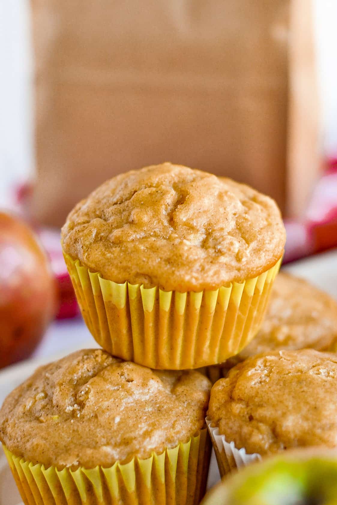 Apple oat muffins stacked in front of a brown paper lunch bag.