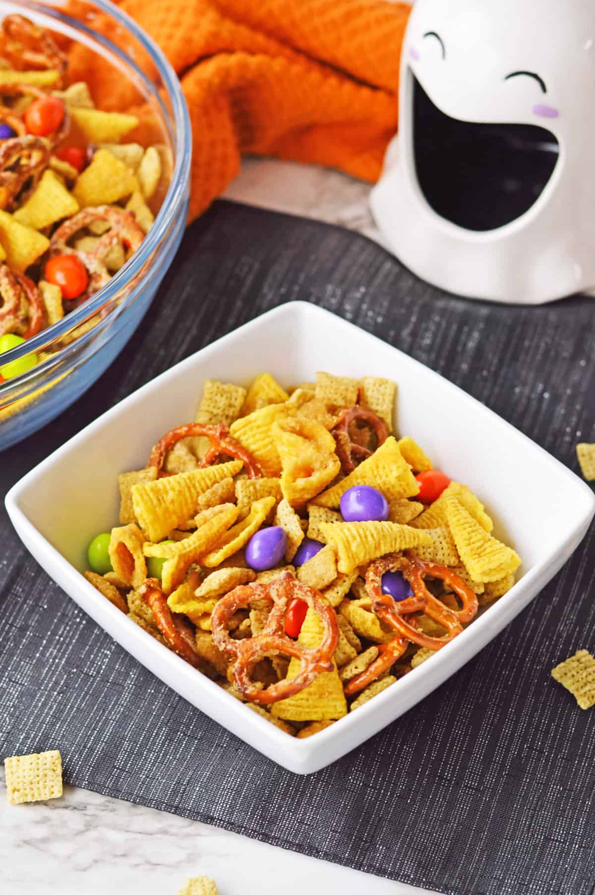 Individual size serving of halloween snack mix in square white bowl.