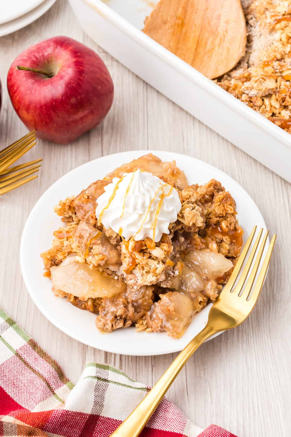 Serving of apple crisp topped with caramel sauce and whipped cream.