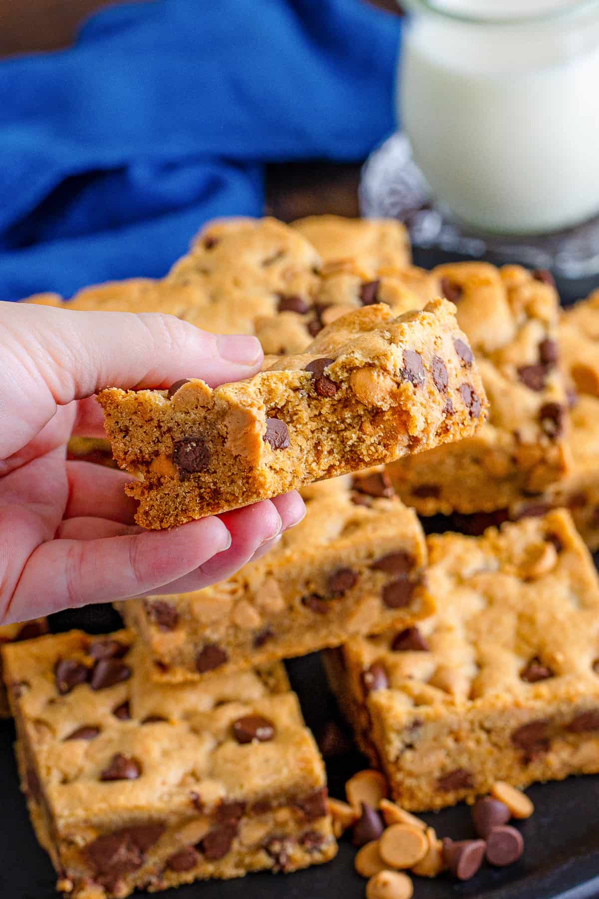 Hand holding cookie bar with bite taken out of it to show chocolate chip and peanut butter chip packed inside.