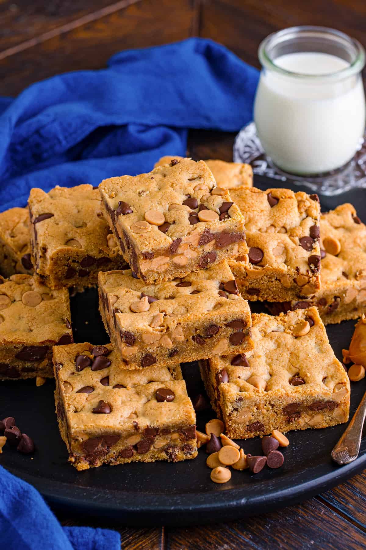 Peanut butter chocolate chip cookie bars on black plate with glass of milk.