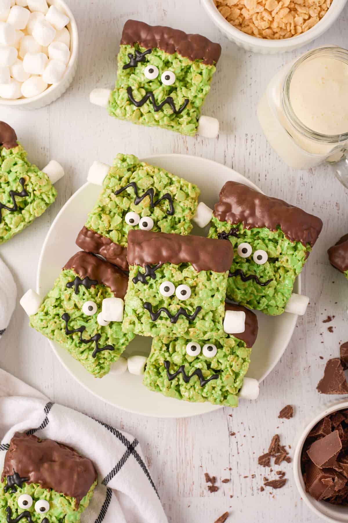 Frankenstein treats piled on white plate with mini marshmallows, chopped chocolate, and other ingredients around them.