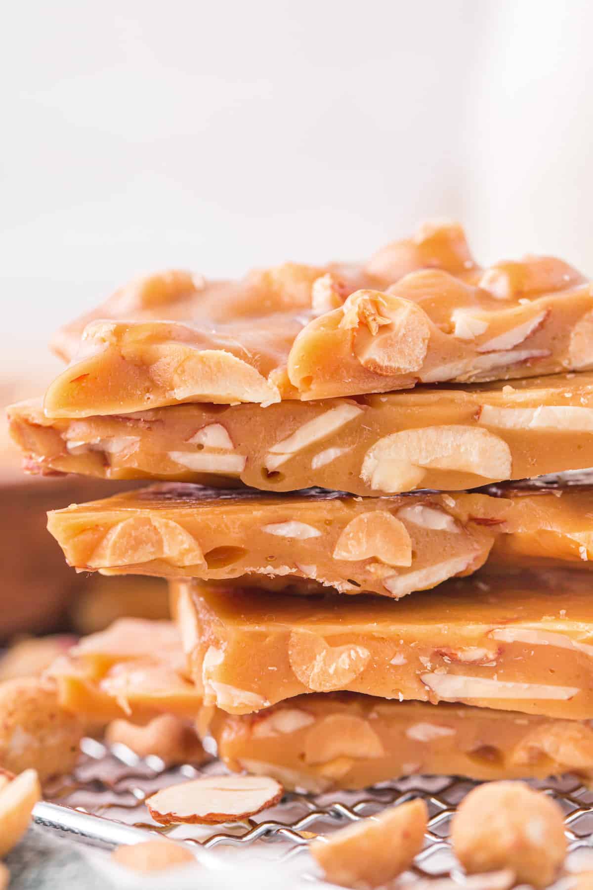 Side view of stack of homemade nut brittle with chunks of almonds and peanuts inside.
