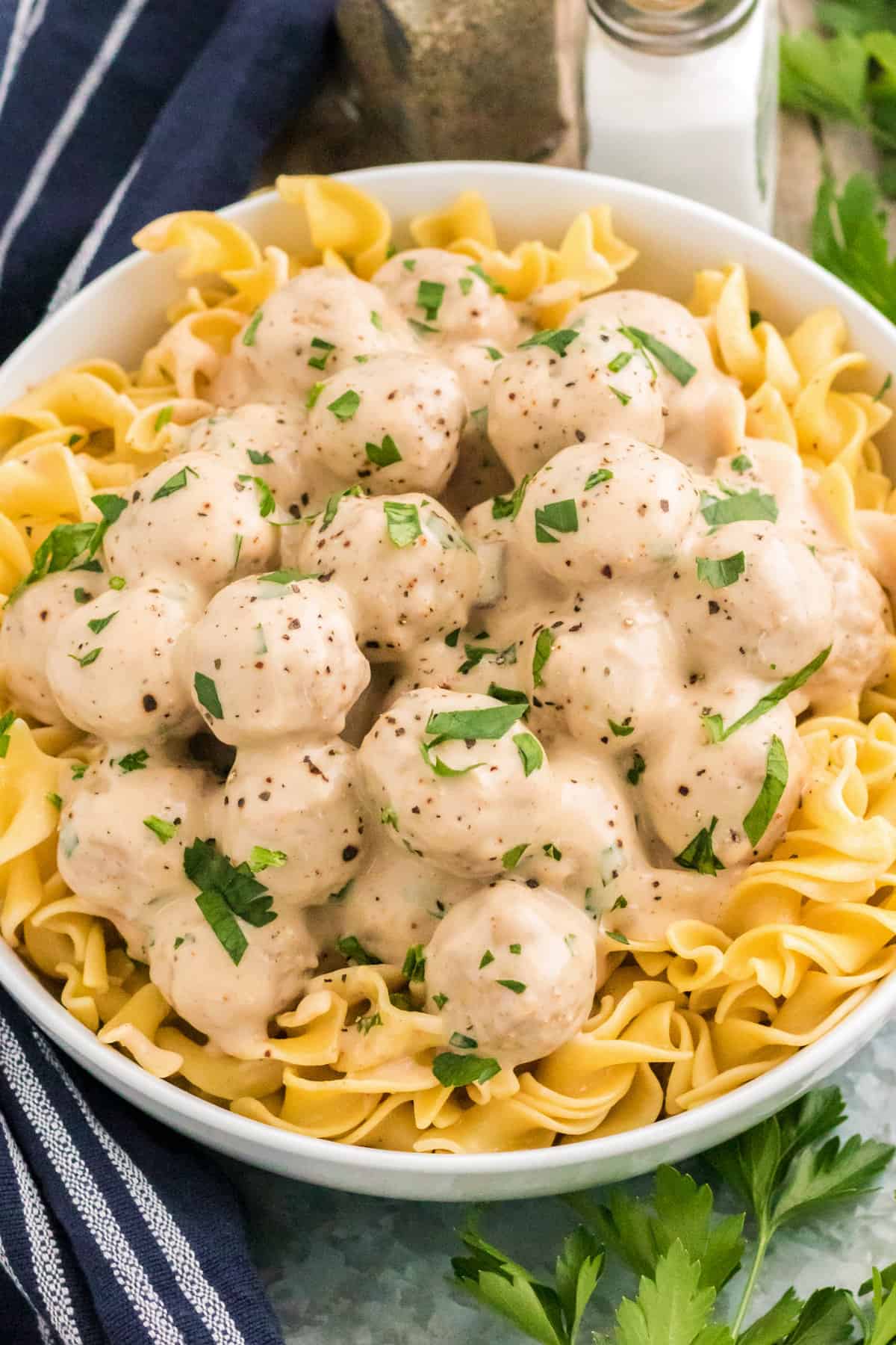 Swedish meatballs and egg noodles in large bowl with salt, pepper, and parsley next to it.