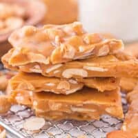 Side view of stack of homemade nut brittle with chunks of almonds and peanuts inside.