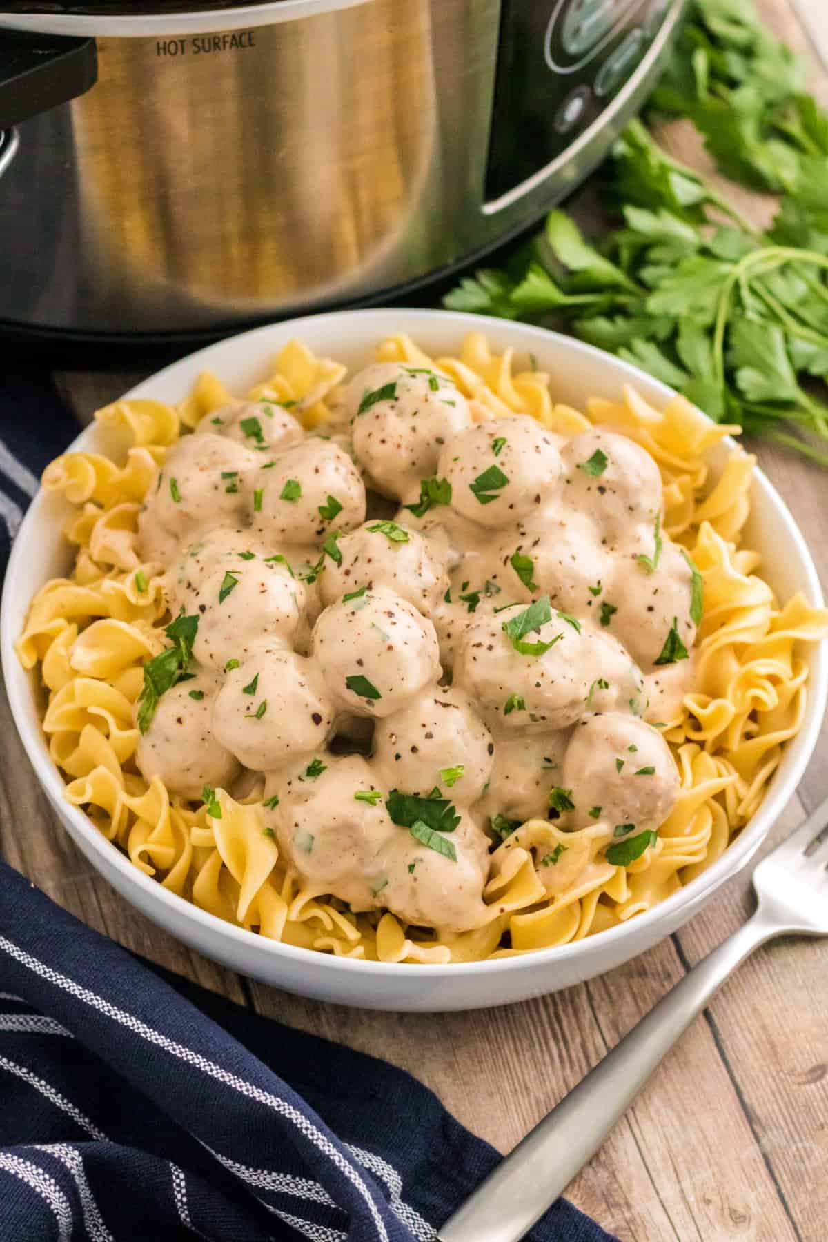 Swedish meatballs served in a bowl over egg noodles with parsley and slow cooker behind them.