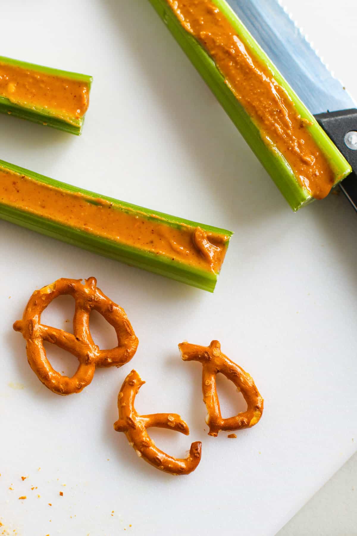 Celery sticks filled with peanut butter next to 2 pretzel twists, once broken in half.