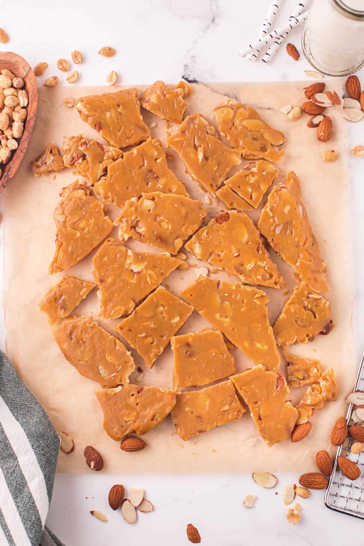 Pieces of nut brittle on parchment paper with almonds and pecans around them.