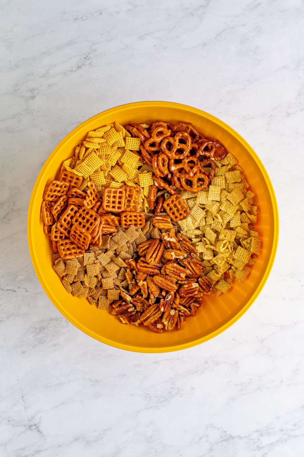 Chex cereal, pecans, and pretzels in a yellow bowl.