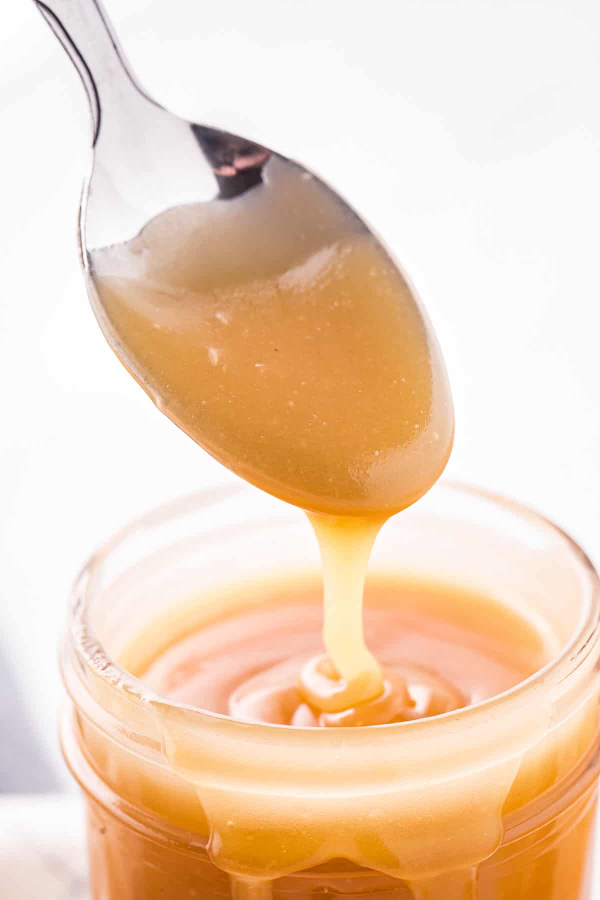 Spoon drizzling caramel sauce into glass jar.