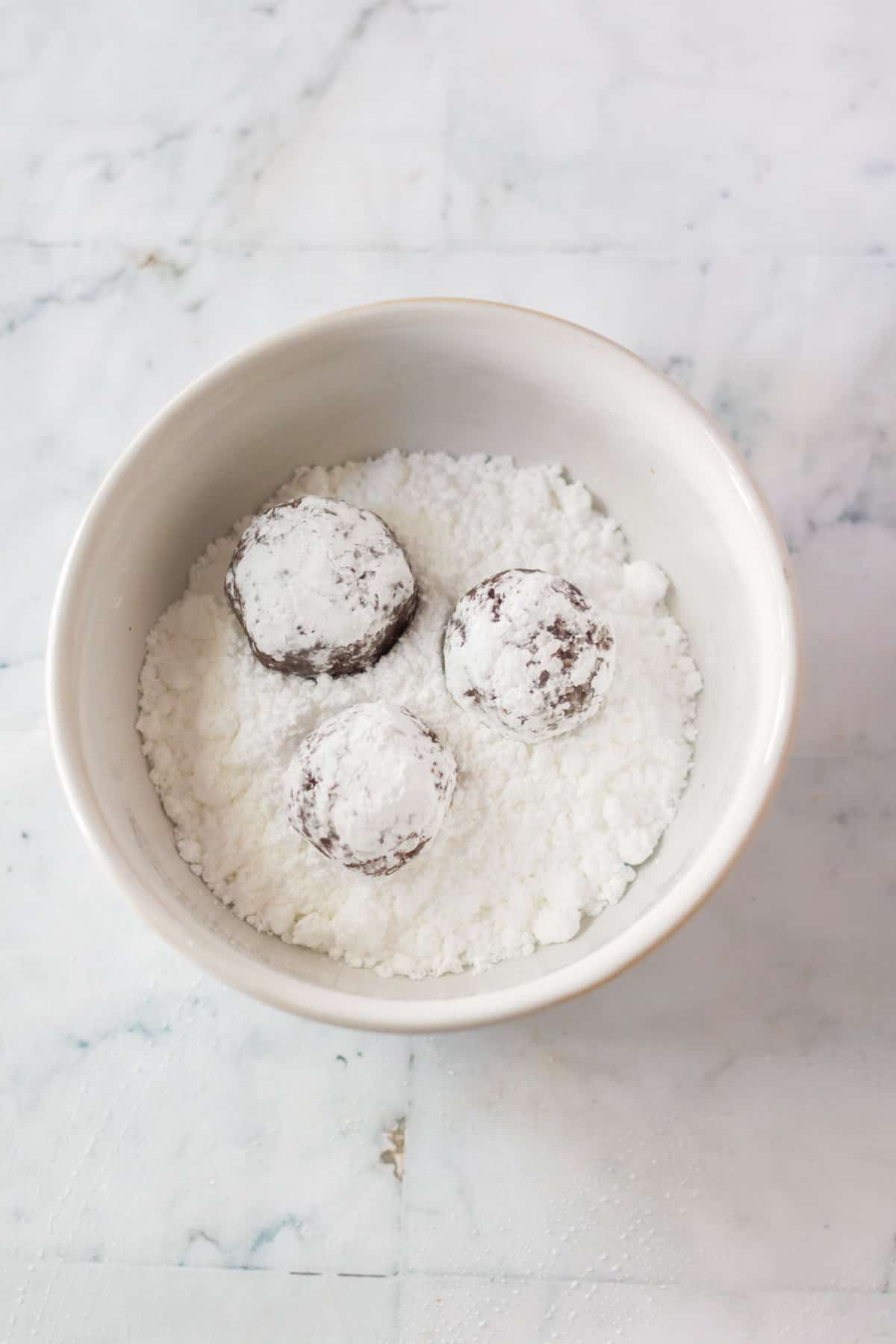 Rum balls being rolled in bowl of powdered sugar.