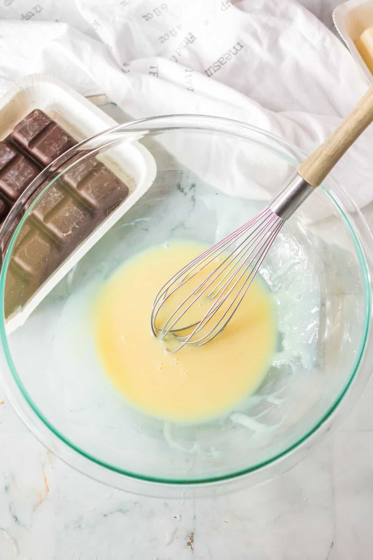 Sweetened condensed milk and peppermint extract combined with a wire whisk in glass mixing bowl.