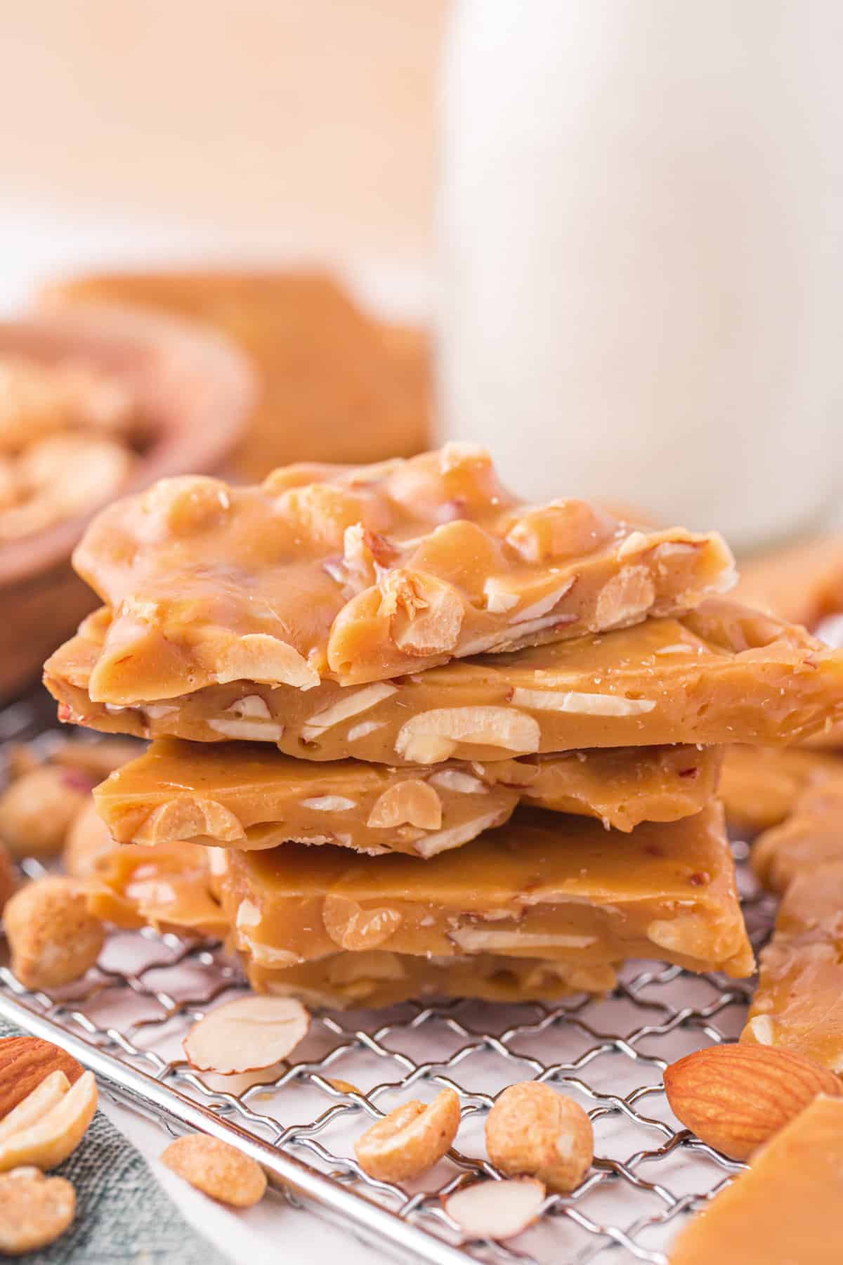 Nut brittle recipe with almonds and peanuts. Roughly broken pieces are stacked in a pile on metal rack.
