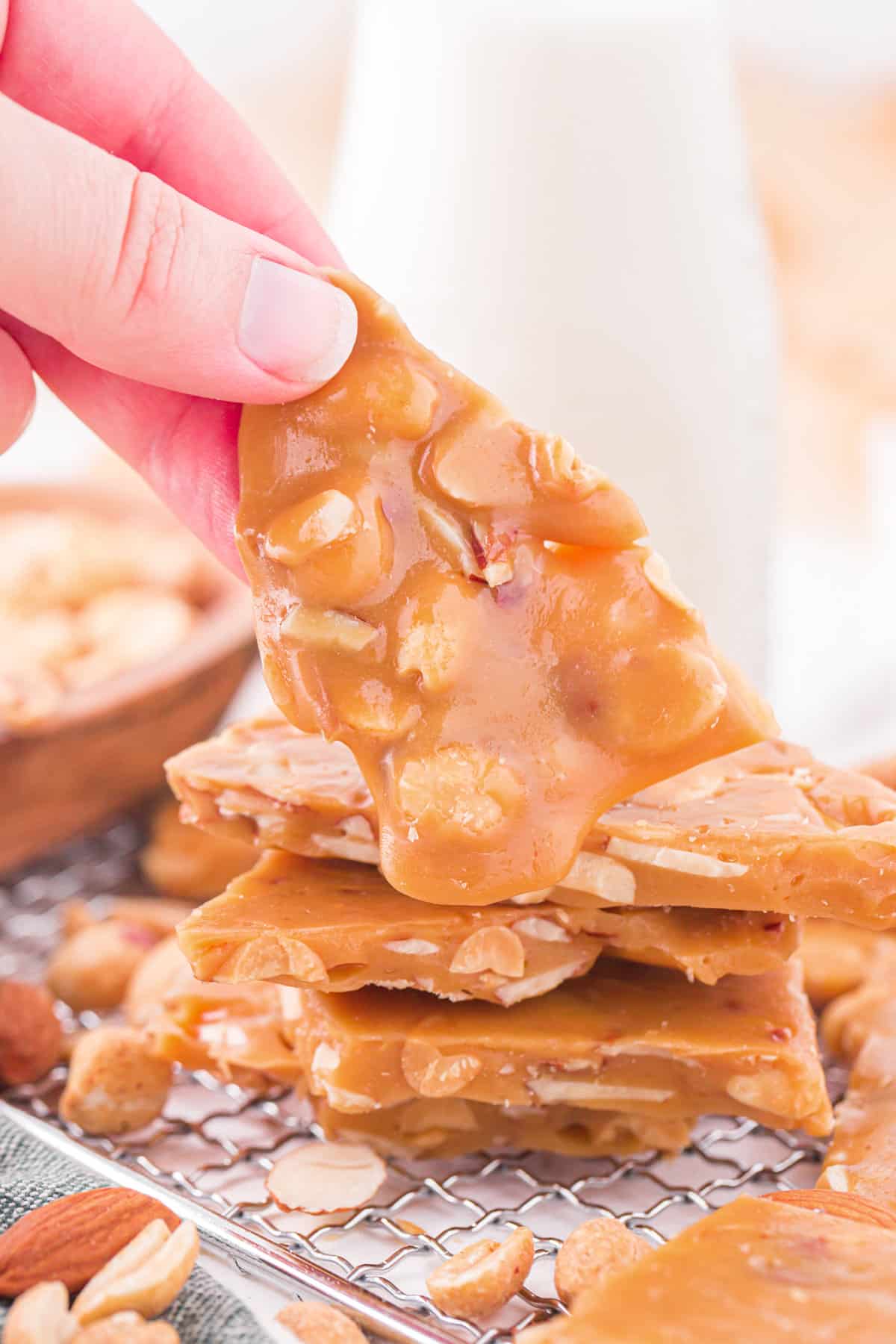 Fingers holding a piece of caramel nut brittle.