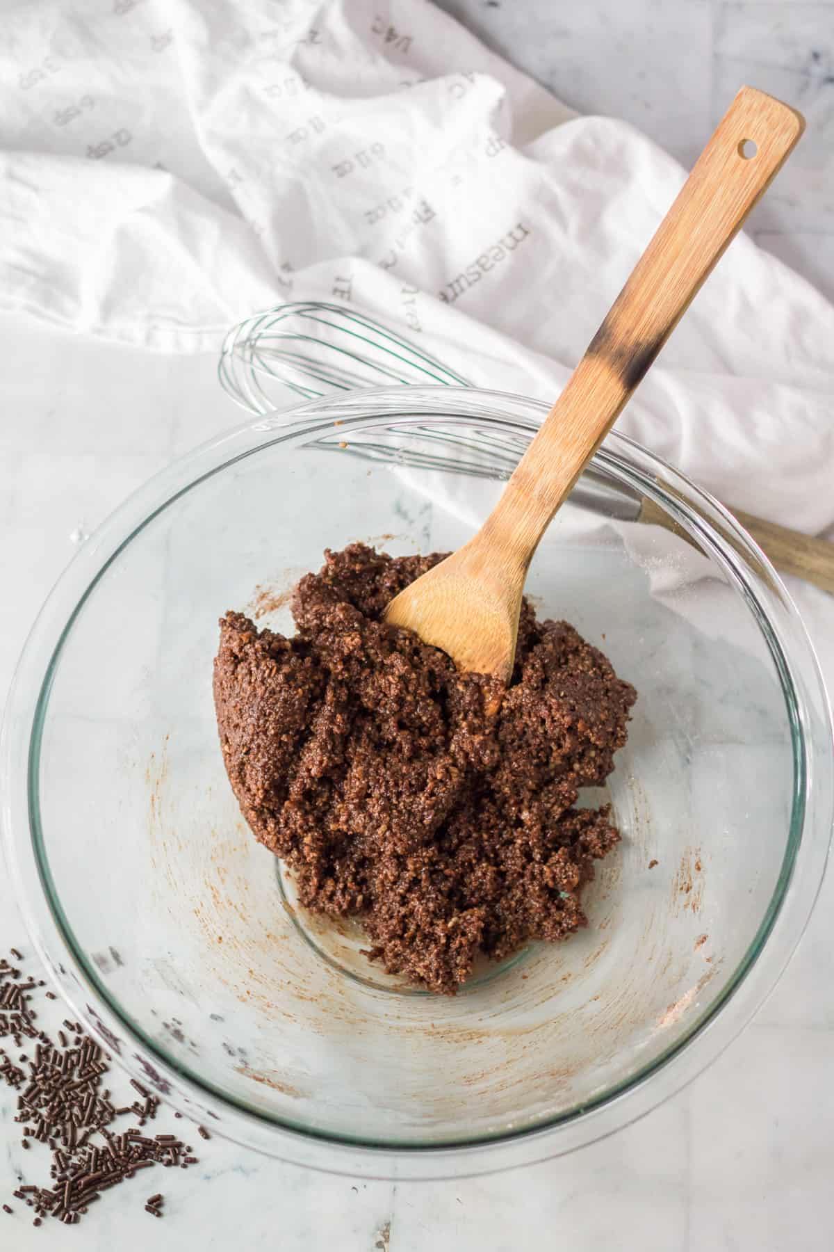 Rum ball dough in glass mixing bowl with wooden spoon.