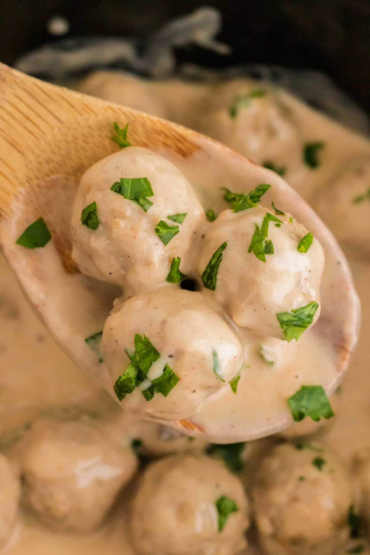 Wooden spoon holding 3 crockpot swedish meatballs.