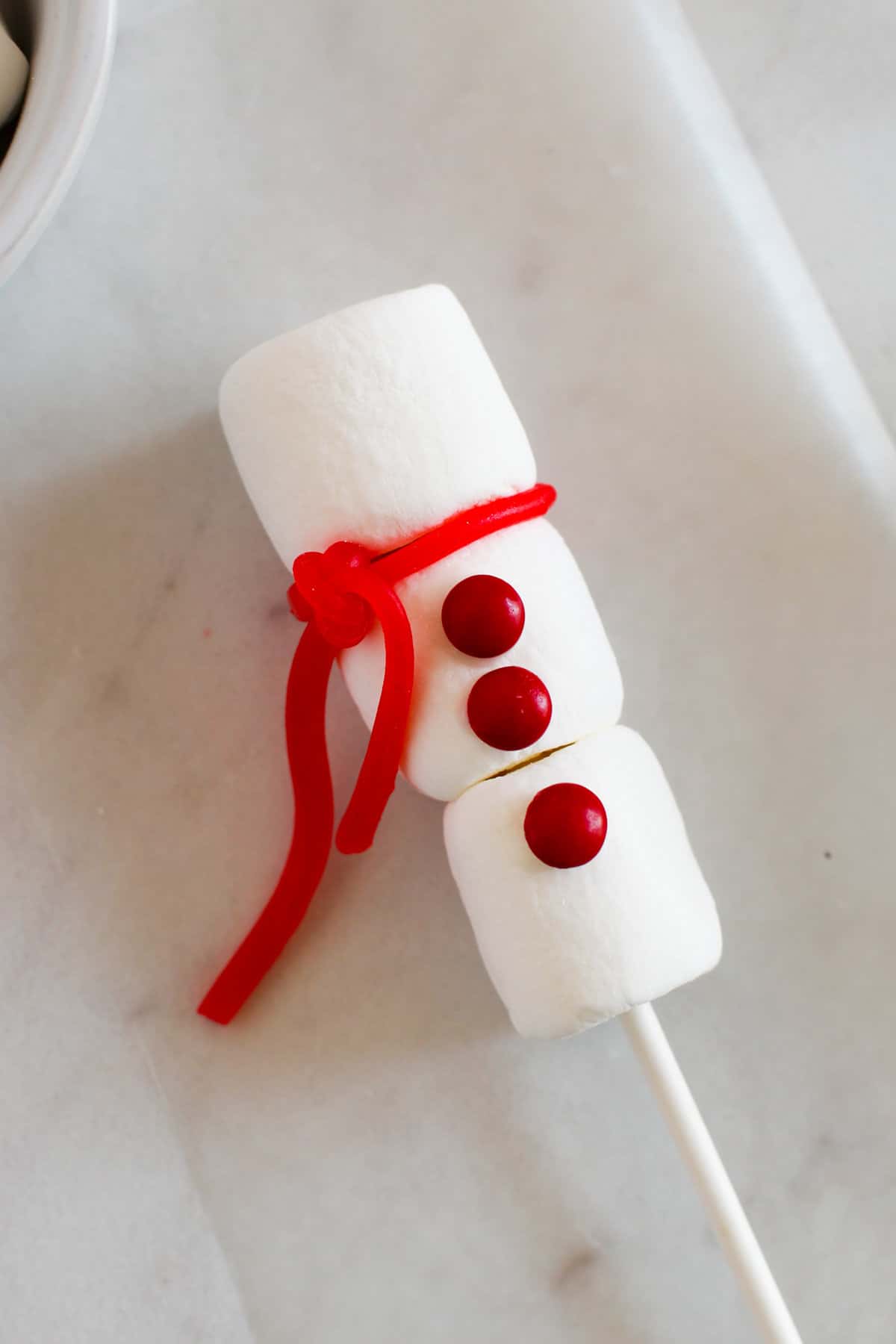 A piece of red candy has been tied between the top and middle marshmallow to make a scarf.