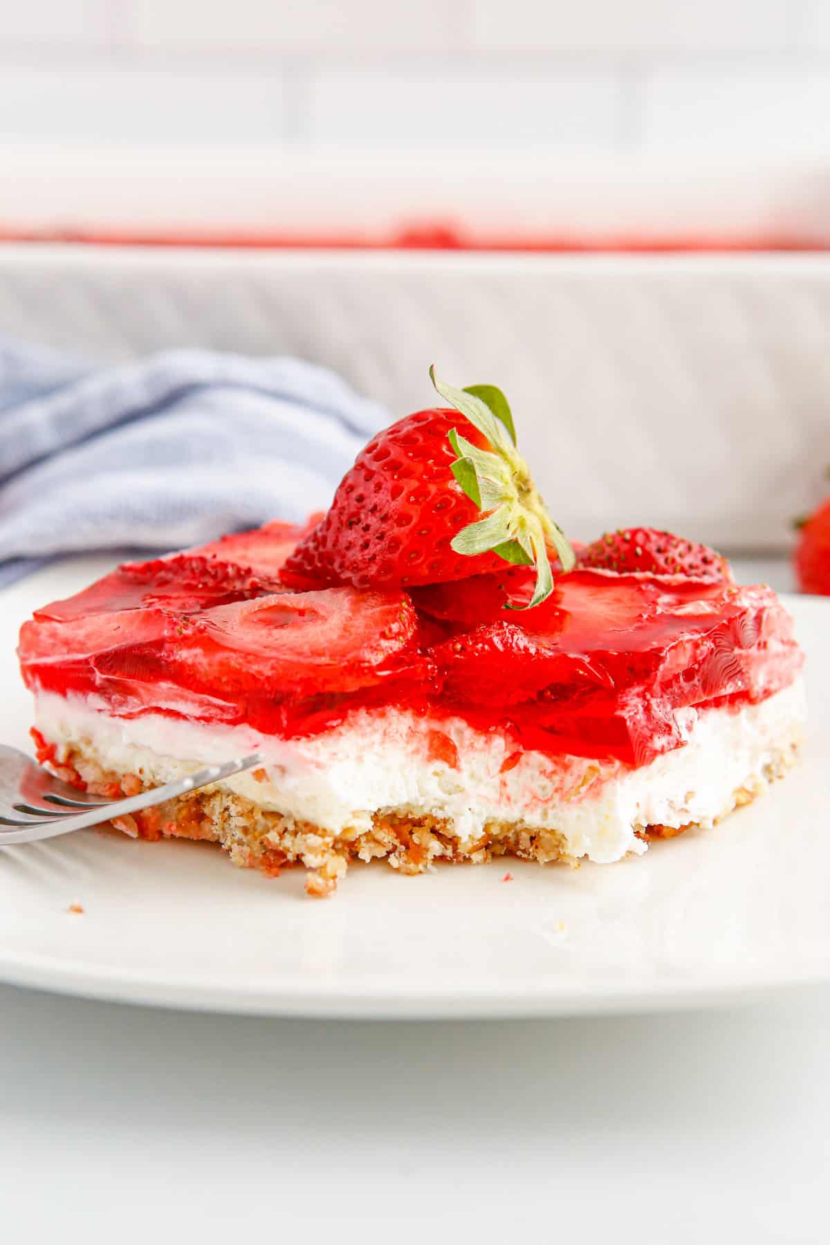 Strawberry pretzel salad on white plate with piece taken out with a fork.