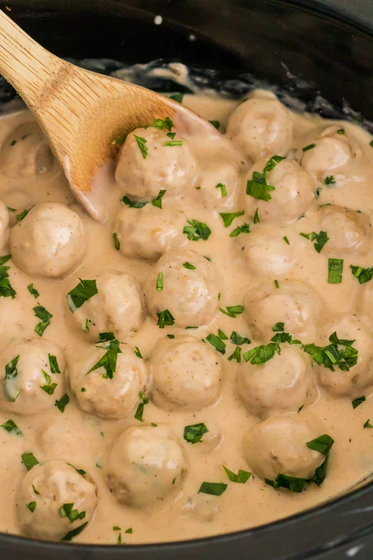 Crockpot Swedish meatballs being stirred with wooden spoon.