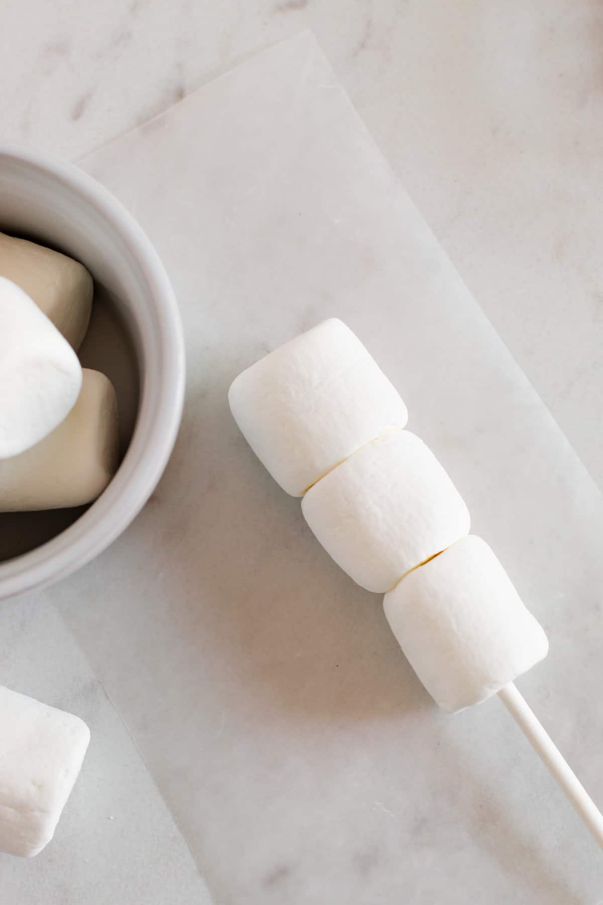 Three white marshmallows on end of white treat stick.